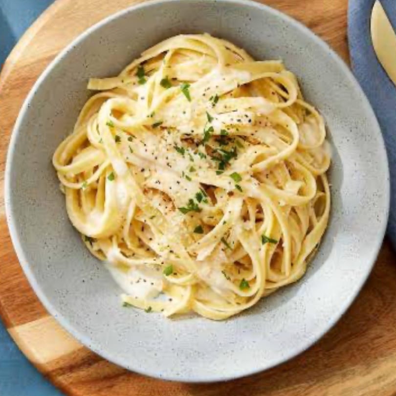 Creamy fettuccine alfredo pasta in a light blue bowl, garnished with parsley and black pepper.