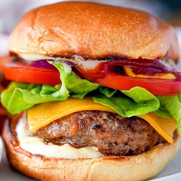 Close-up of a juicy burger with melted cheese, fresh lettuce, tomato, and red onion on a brioche bun.